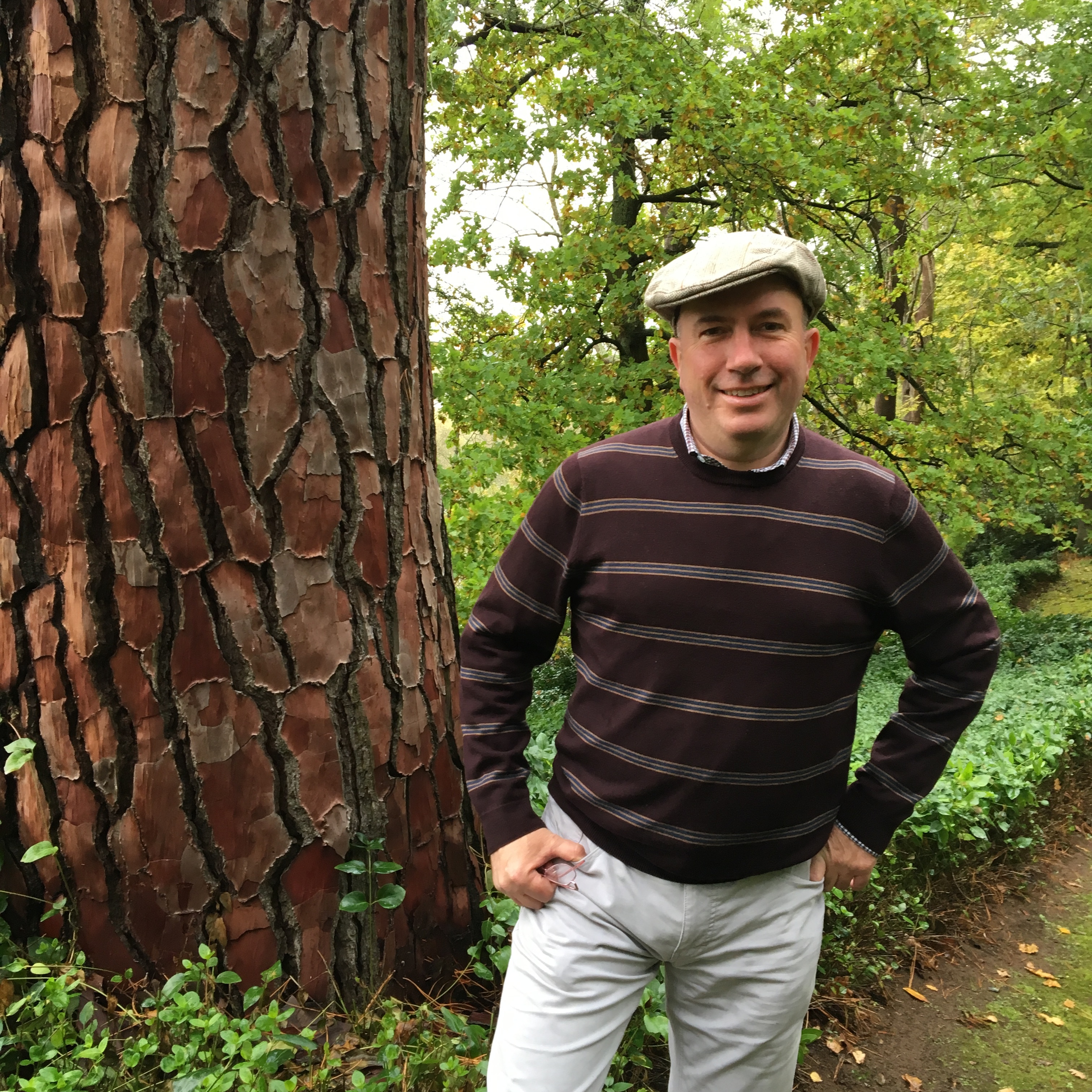 A man stands next to a tree, in a forested area.