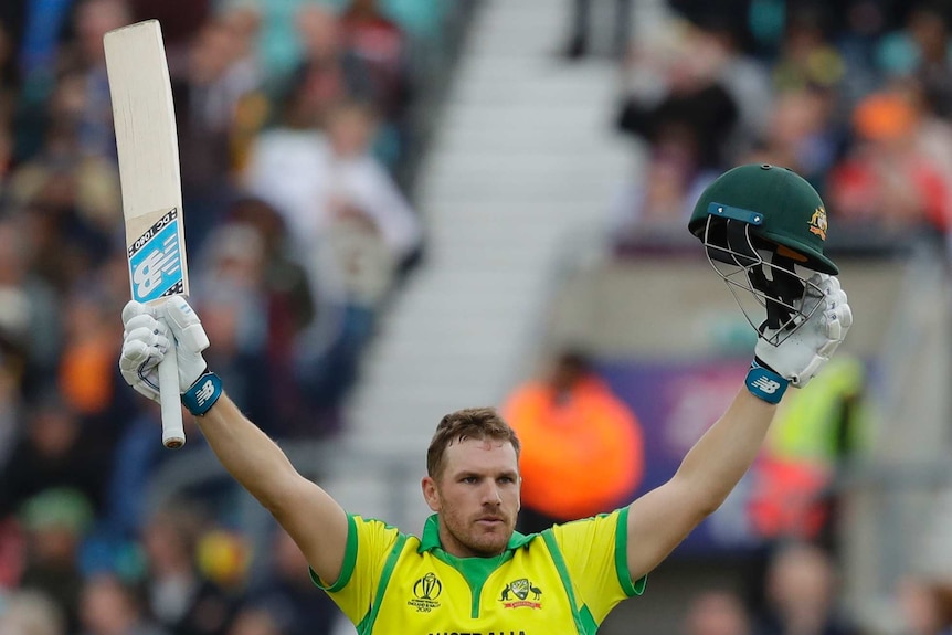 Aaron Finch puts his hands up with his bat in one hand and helmet in the other