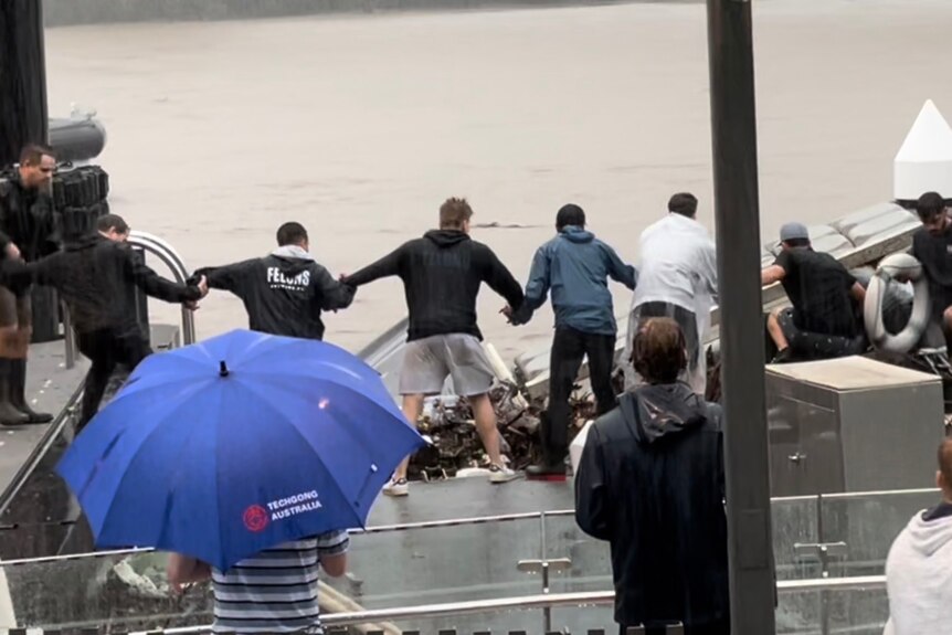 People link arms in the rain as they conduct a rescue on the Brisbane River.