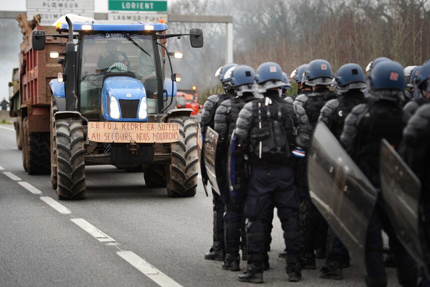 French riot police stand on a motorway facing protesters in a tractor.