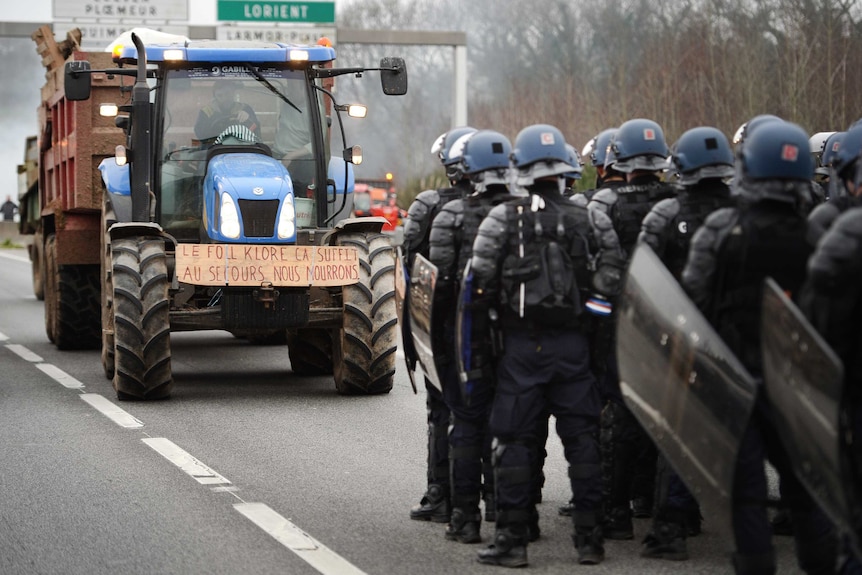 French riot police stand on a motorway facing protesters in a tractor.