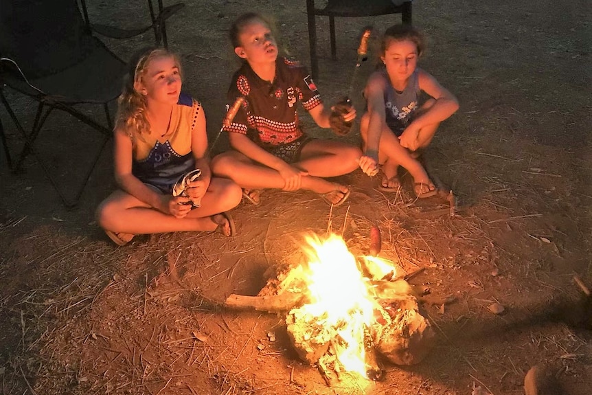 Three young girls sitting around a campside campfire in twilight