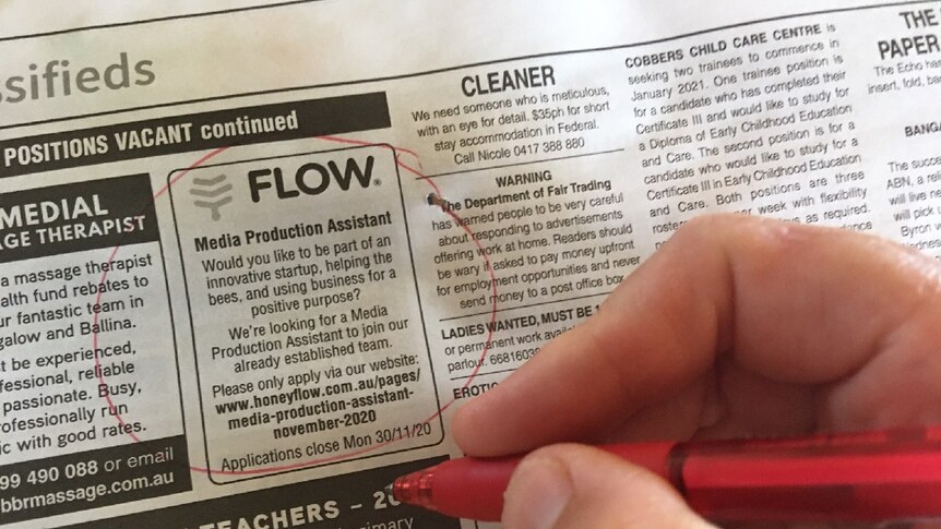 A positions vacant newspaper page with a hand holding a red pen and circling jobs