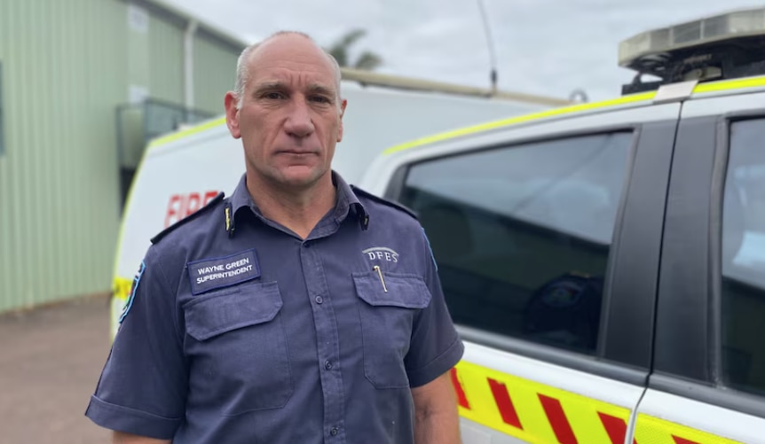 Wayne Green, de camisa azul, está na frente de um veículo.