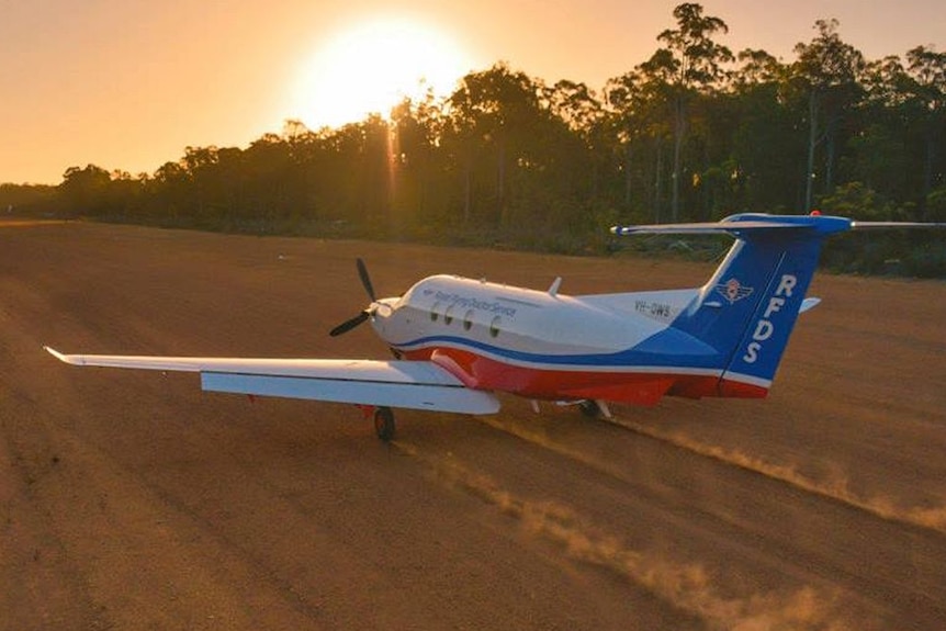 A red, white and blue Royal Flying Doctor Service B200 Super King Air landing on a Queensland outback airstrip