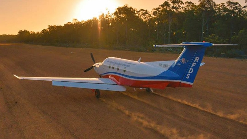 A small plane rolling down a dirt airstrip with dust kicking up behind its wheels.