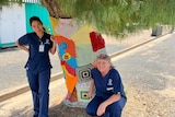 two nurses in front of a tree wrapped in wool