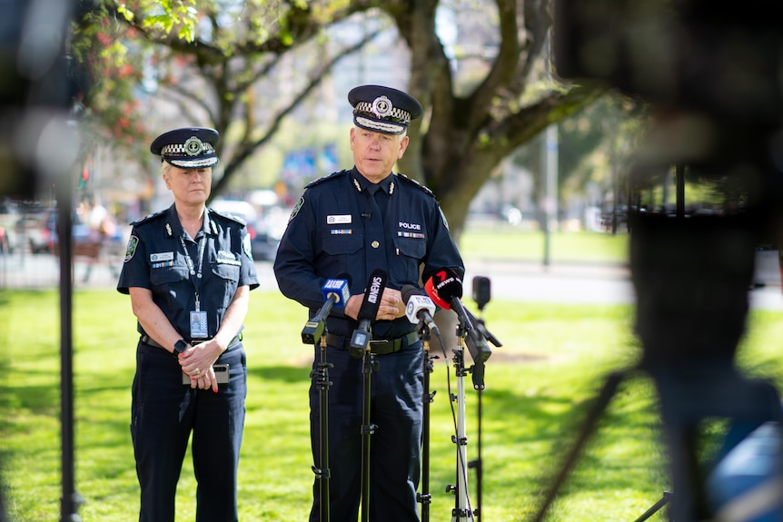 A police officer speaks into microphones on a stand in a park