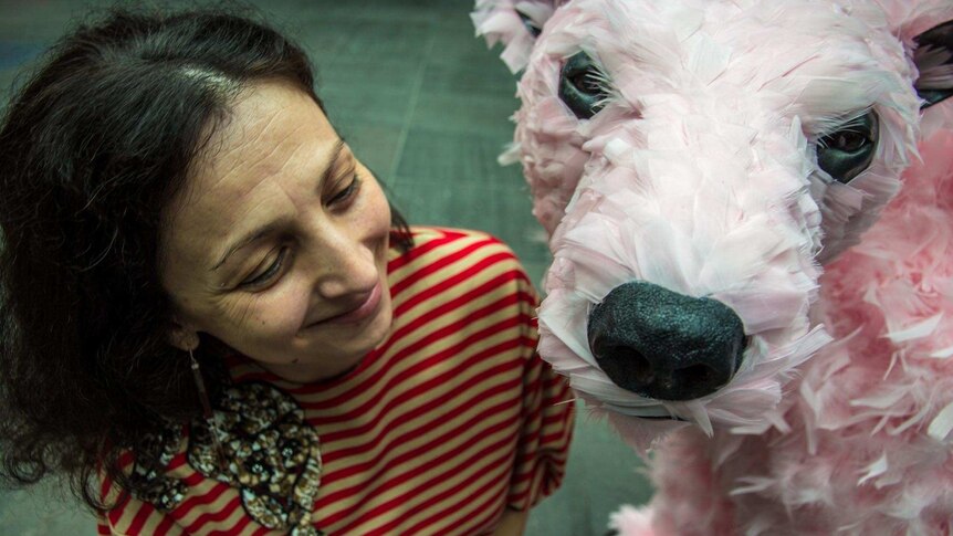 A woman looks at a sculpture of a pink neon feathered bear