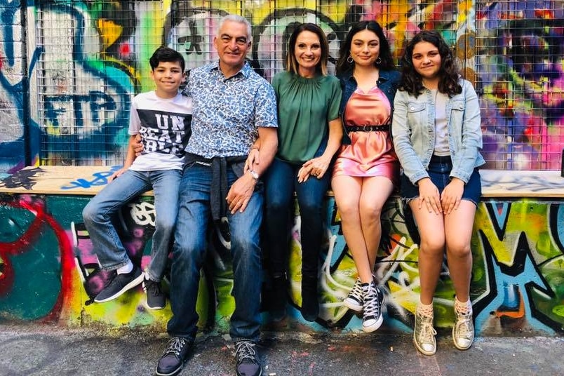 A family sitting in front of a graffiti wall smiling for the camera