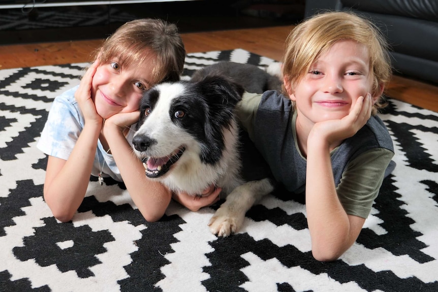 Mira Jung, 7, dog Molly, and Fynn Goat, 8, posing on the rug in a living room on school holidays