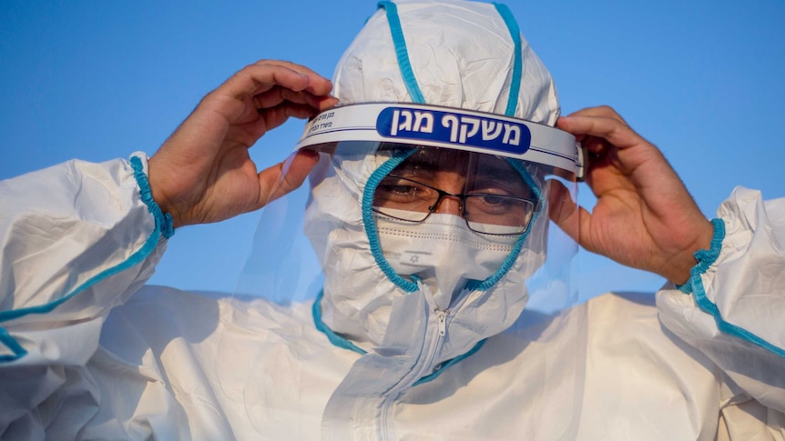 A man in full PPE with Hebrew writing across the top of his face guard