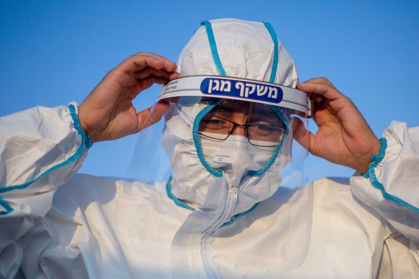 A man in full PPE with Hebrew writing across the top of his face guard