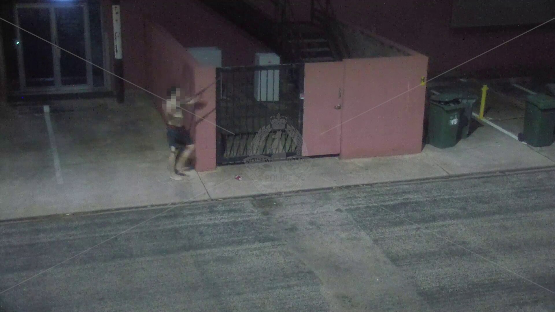 Man holding a long gun in front of pink building. 