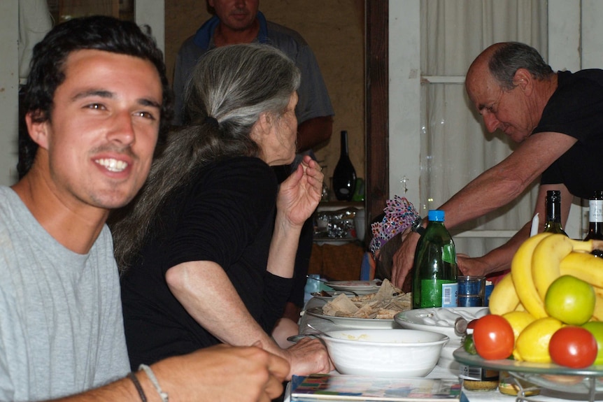 A smiling Jarrod Hampton face sthe camera while sitting at the dinner table with family members in the background.