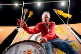 Fred Brophy, in a red shirt, bangs on a drum outside an orange tent.