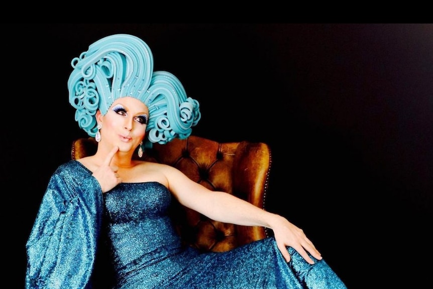 Drag queen in sparkly blue gown with large curly blue wig