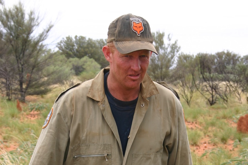 A man wearing beige overalls is photographed in the bush