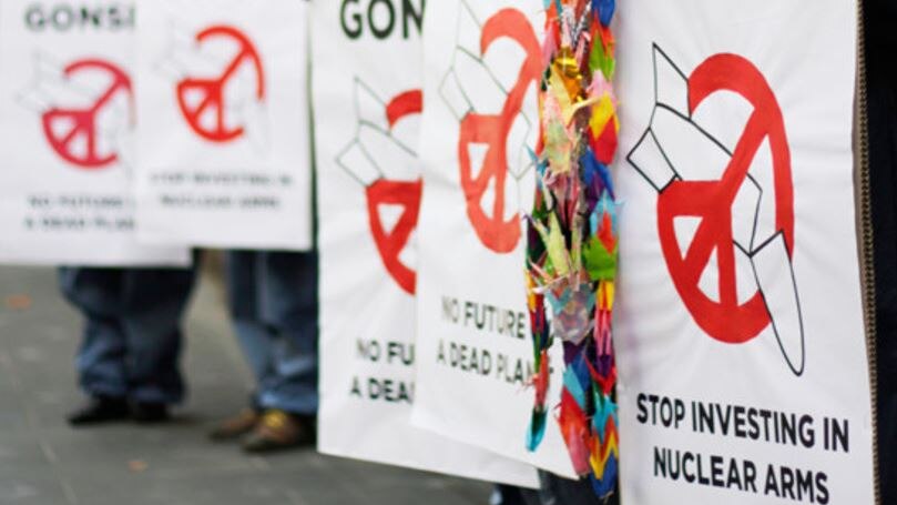 Shot of a line of protestors holding graphic images of broken nuclear missiles in red peace sign shaped 'banned' circles