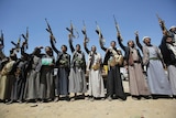 A line of tribesmen hold their weapons straight in the air as they chant slogans.