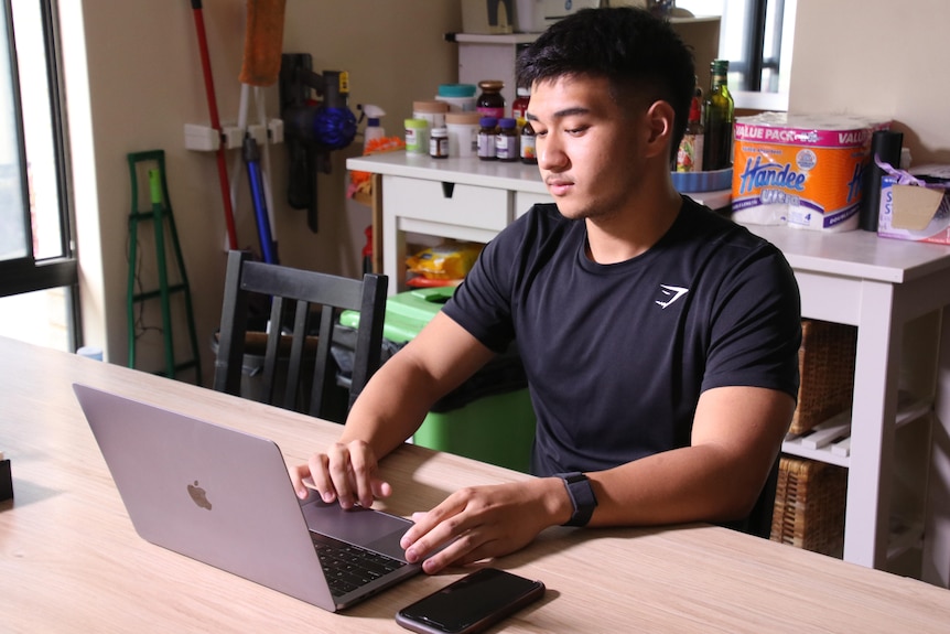 A young man at a kitchen table in front of an open laptop