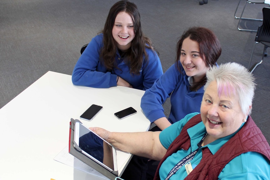 Two female high school students sit next to a 66-year-old woman holding an eye pad