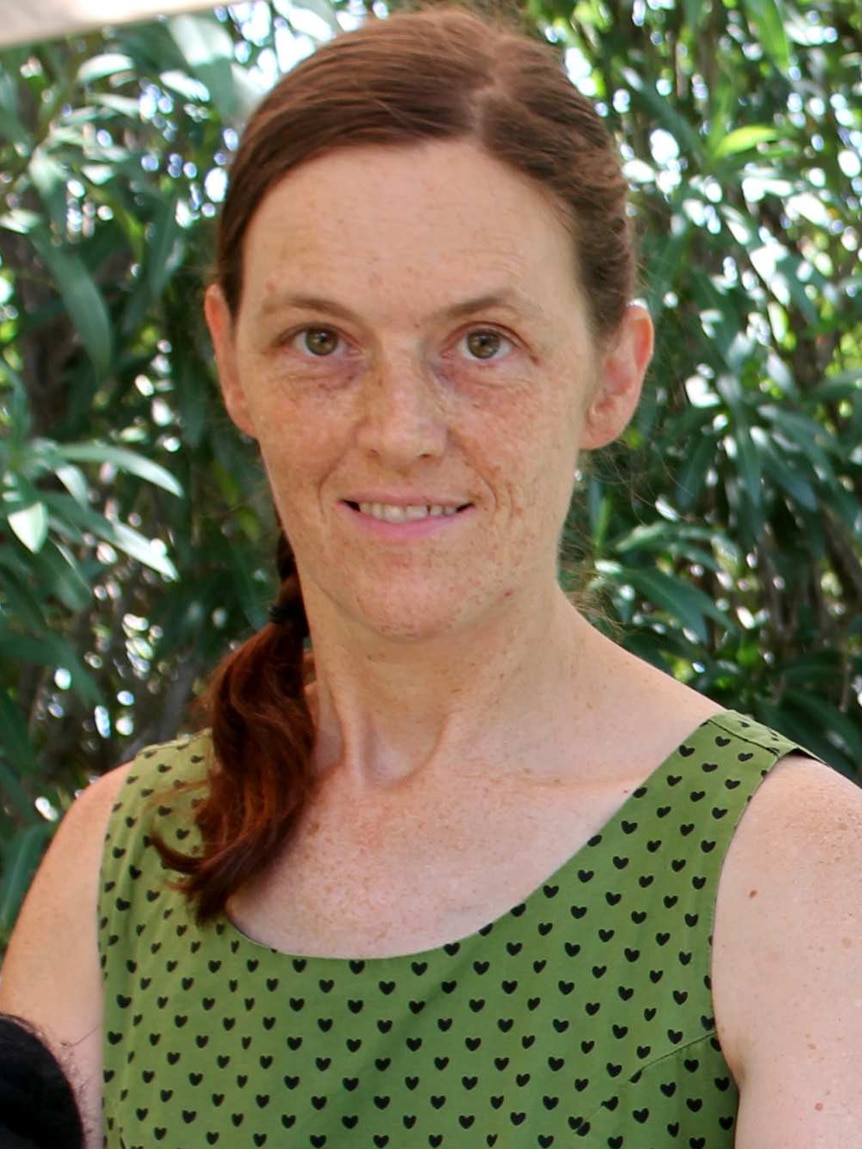 A close-up on a woman with medium length red hair, wearing a green top.