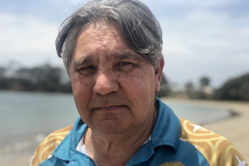 a man stands looking at the camera with a lake in the background.