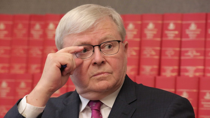 Kevin Rudd readjusts his glasses while sitting in front of red books of legislation