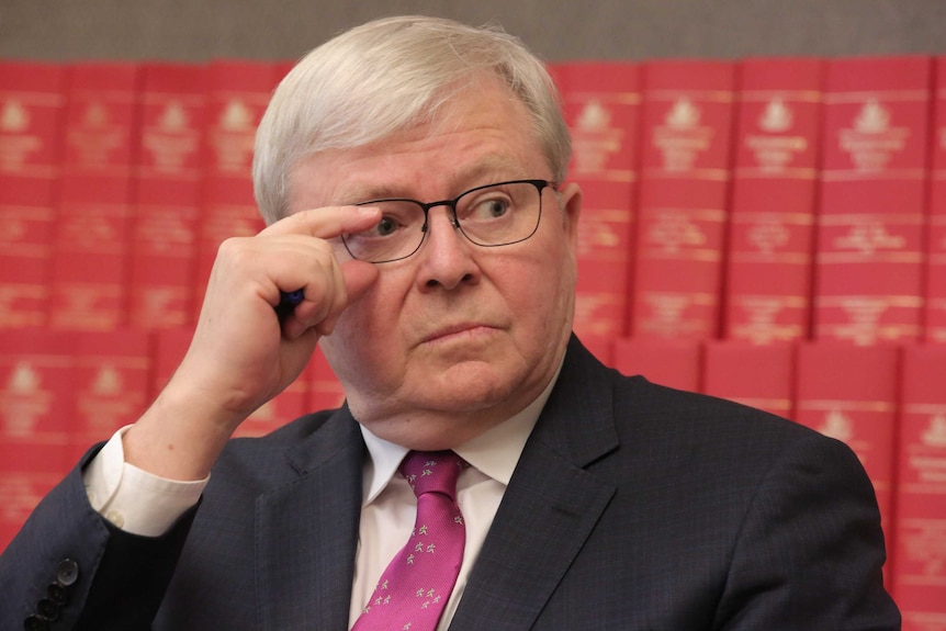 Kevin Rudd readjusts his glasses while sitting in front of red books of legislation