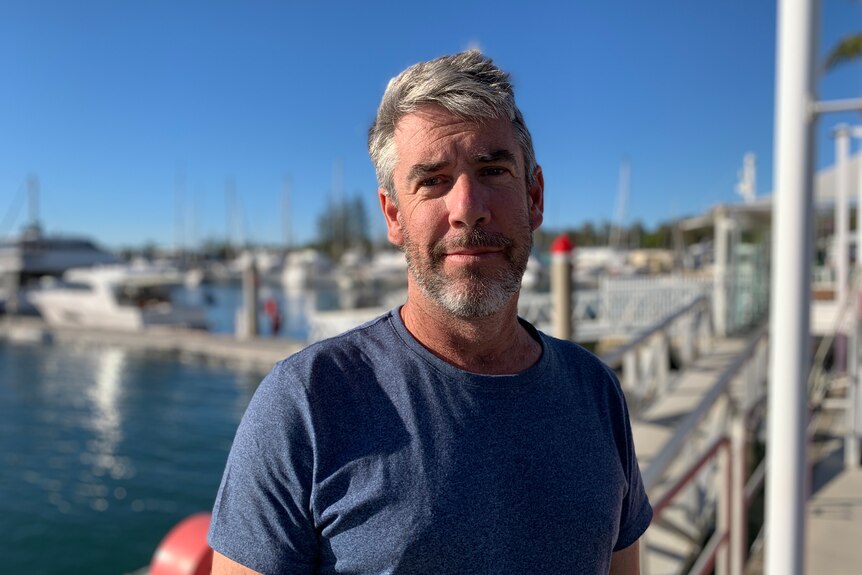 Lee Randall in a blue shirt standing near on a wharf looking at the camera