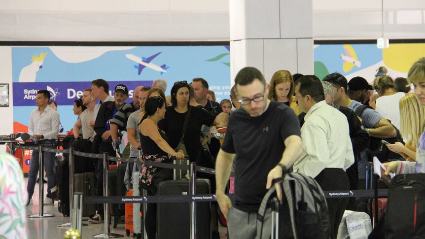 A crowd of people line up with luggage