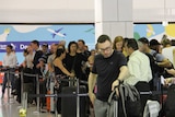 A crowd of people line up with luggage