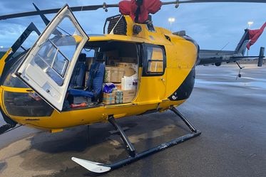 A yellow helicopter on the ground with the door open.