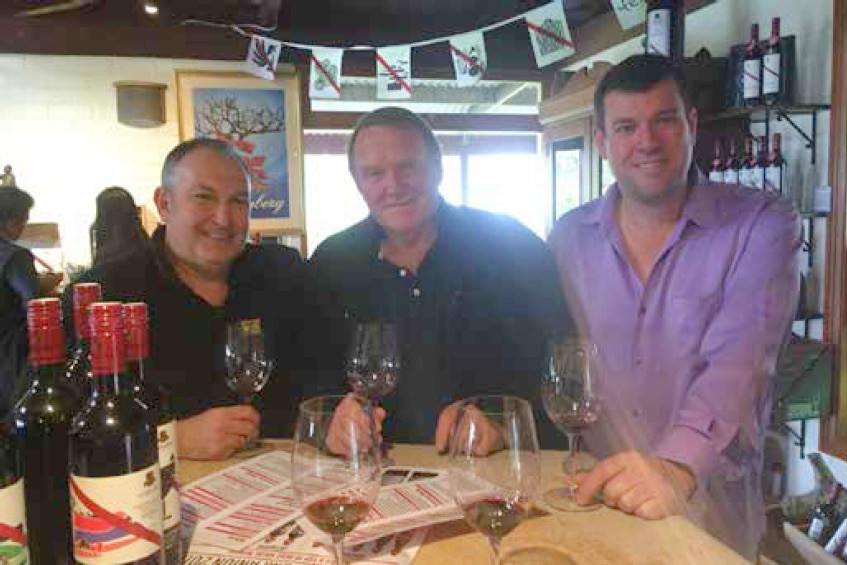 Three men posing for a photo at a table at a winery