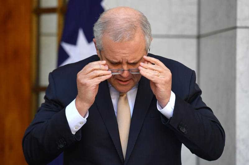 prime minister scott morrison adjusts his reading glasses while looking down