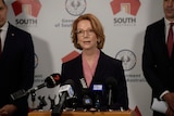 Julia Gillard, a red-headed woman in a suit, speaks at microphones during a press conference.