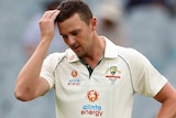 Josh Hazlewood puts his hand on his head and looks downwards. An umpire watches on in the foreground