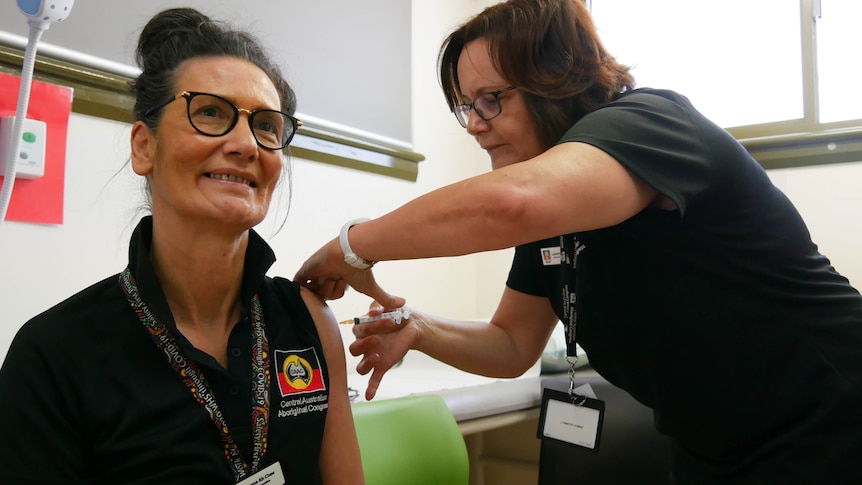 Donna Ah Chee, a woman, smiling as she receives a COVID-19 vaccine in her left arm.