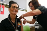 Donna Ah Chee, a woman, smiling as she receives a COVID-19 vaccine in her left arm.