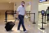 US Senator Ted Cruz, wearing a Texas flag face mask, carrying luggage through an airport.