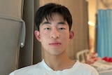 Rong Shi sits in a hospital ward room in a white t-shirt.