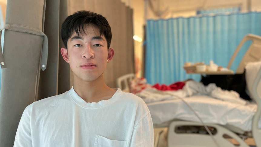 Rong Shi sits in a hospital ward room in a white t-shirt.