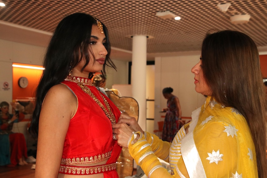 A designer adjusts a model's outfit backstage at a fashion show