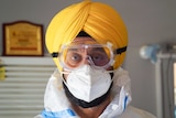 A Sikh man in a yellow turban and full PPE including goggles and a mask