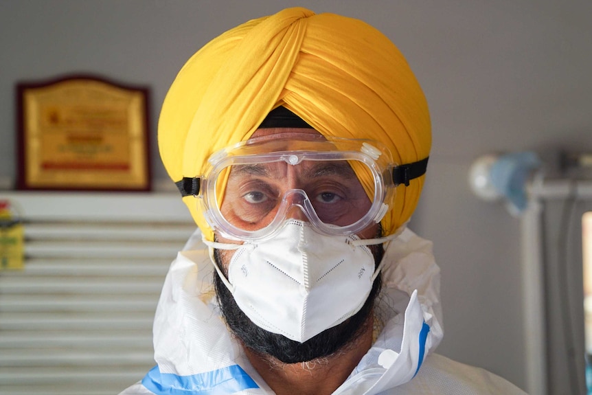 A Sikh man in a yellow turban and full PPE including goggles and a mask