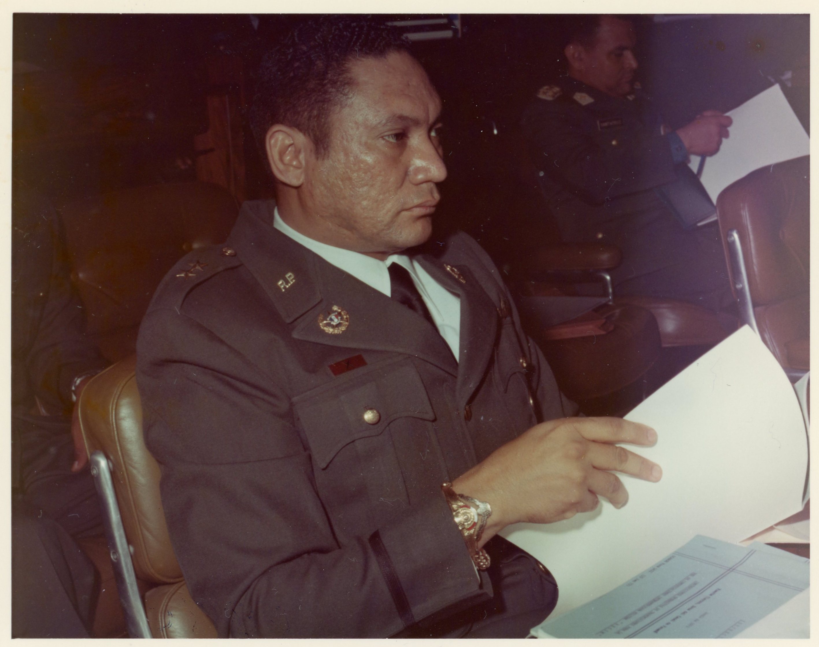 a man in military uniform sits with a stern expression holding papers 