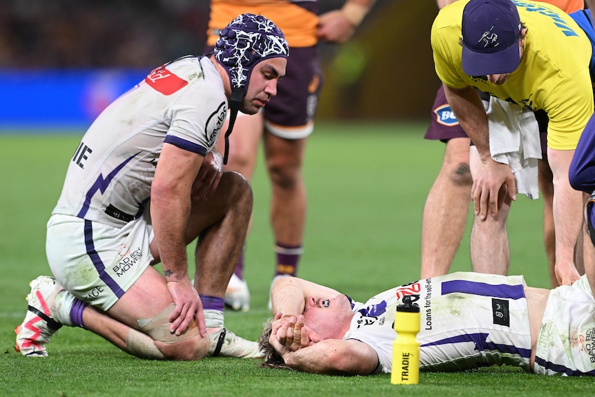 Melbourne Storm's Jahrome Hughes kneels over teammate Ryan Papenhuyzen after an injury in an NRL clash with Brisbane.