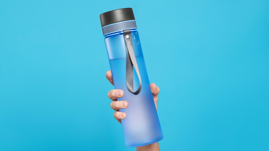 Woman holding bottle of drink on light blue background, closeup