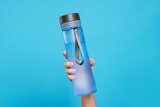 Woman holding bottle of drink on light blue background, closeup.